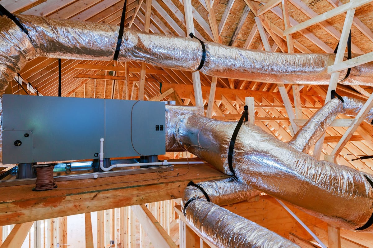 Workers installing ductwork for a heating and cooling system in a home under construction